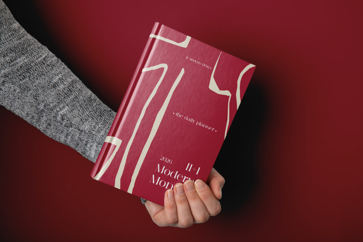 Hand holding a red planner with white text on a dark red background