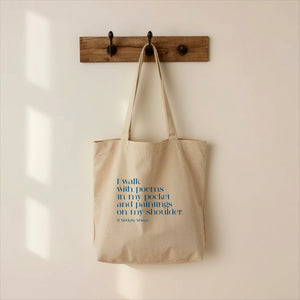 Beige tote bag with text hanging on a wooden hook against a beige wall