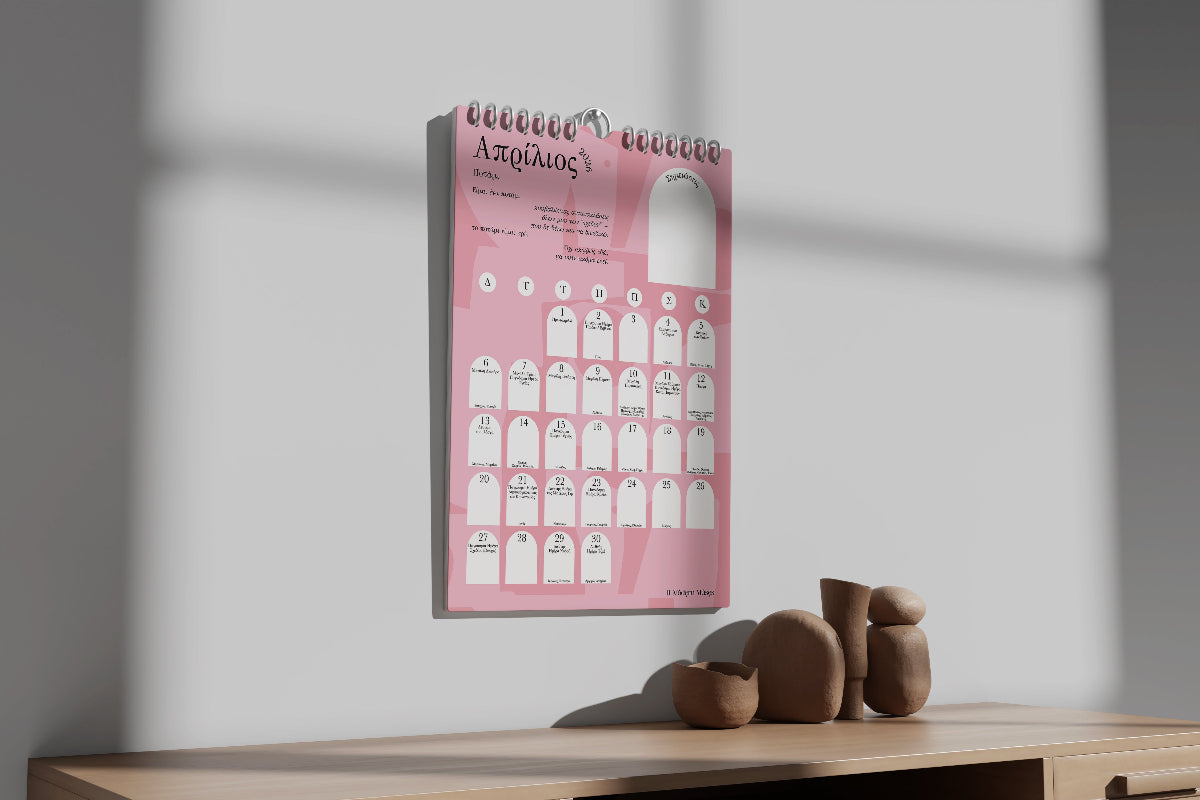 Pink and black spiral-bound wall calendar on a wooden surface with a white wall background