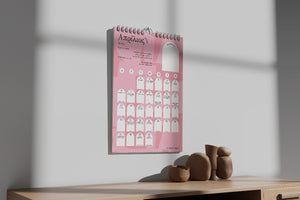 Pink and black spiral-bound wall calendar on a wooden surface with a white wall background