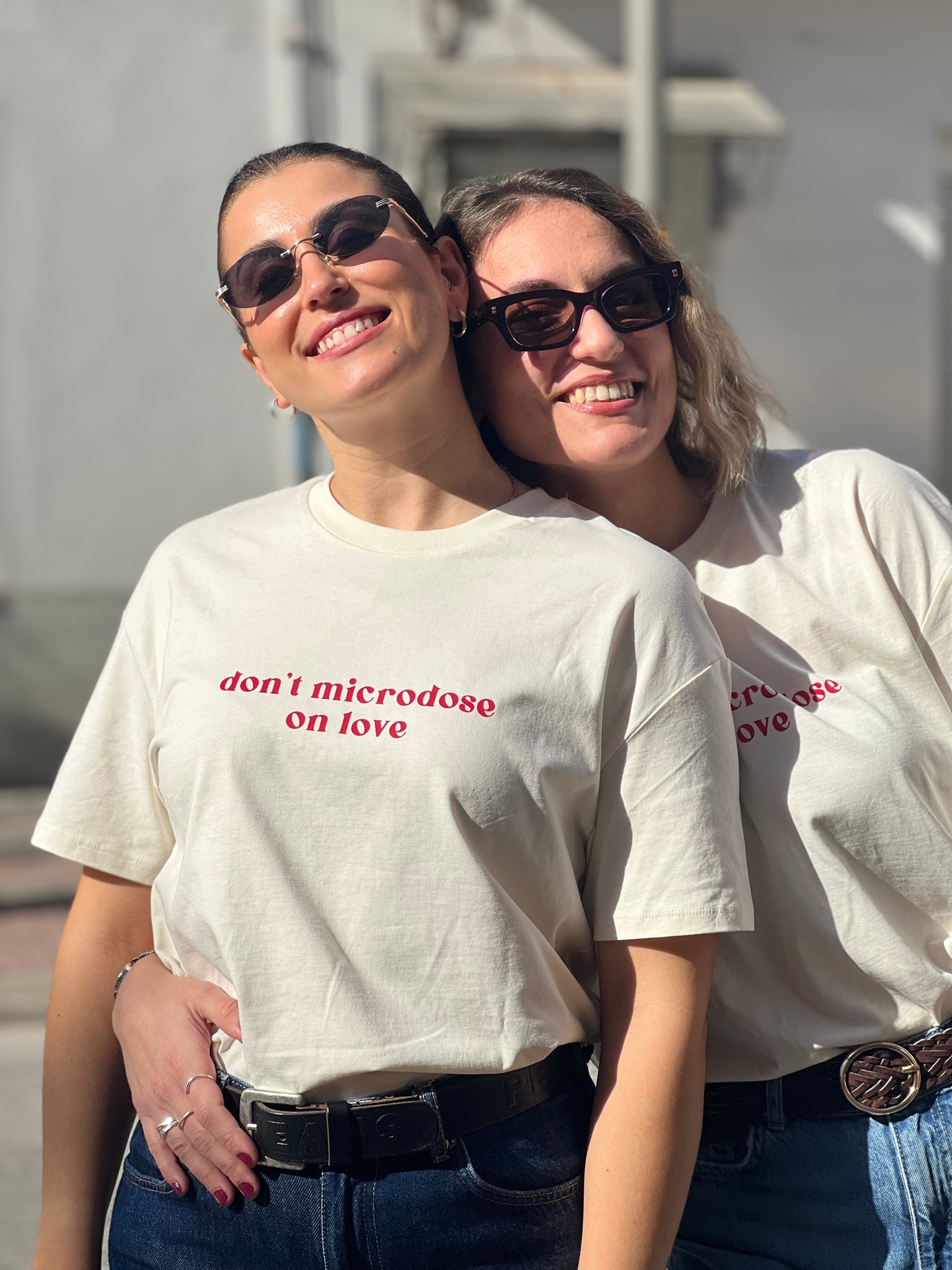 Two people wearing matching t-shirts with the message "don't microdose on love", standing close together outdoors in Patras 