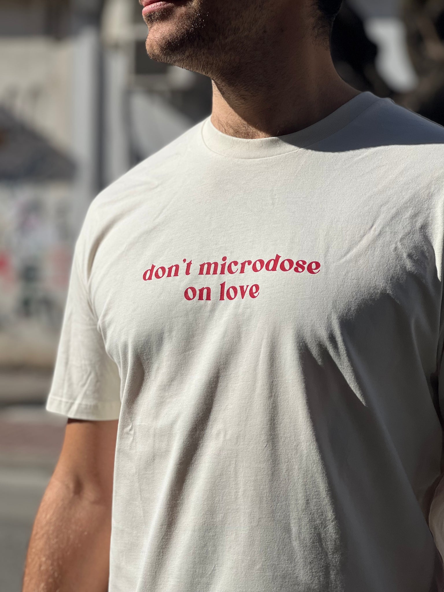 Person wearing a white t-shirt with red text 'don't microdose on love' in an urban setting.