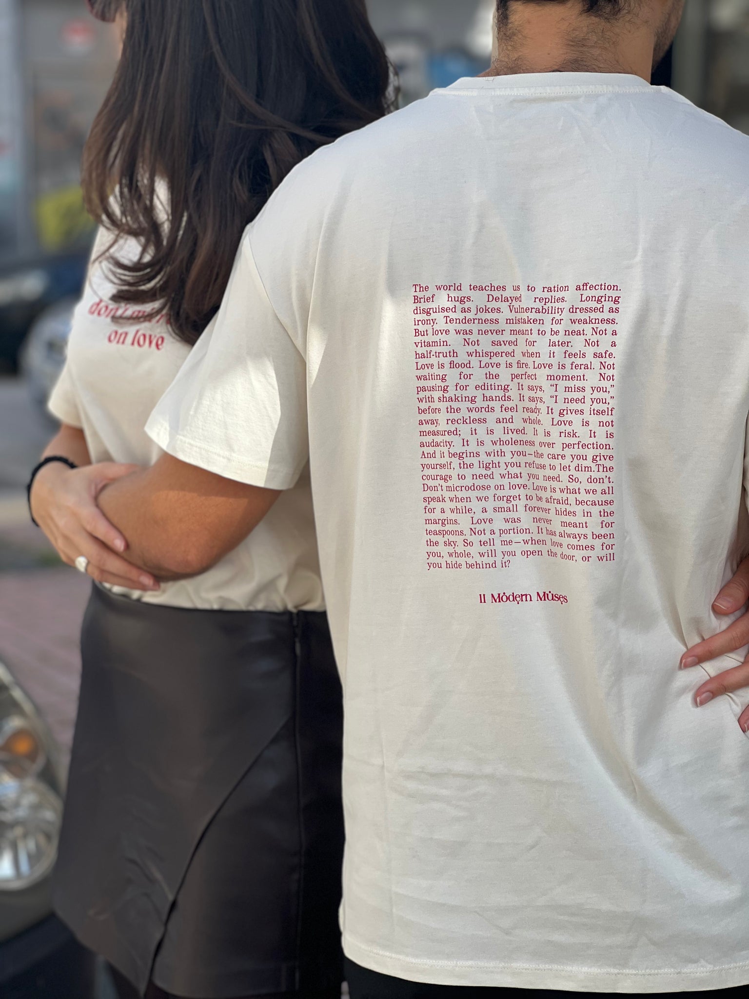 A couple wearing white t-shirts with text on the back, standing close together.