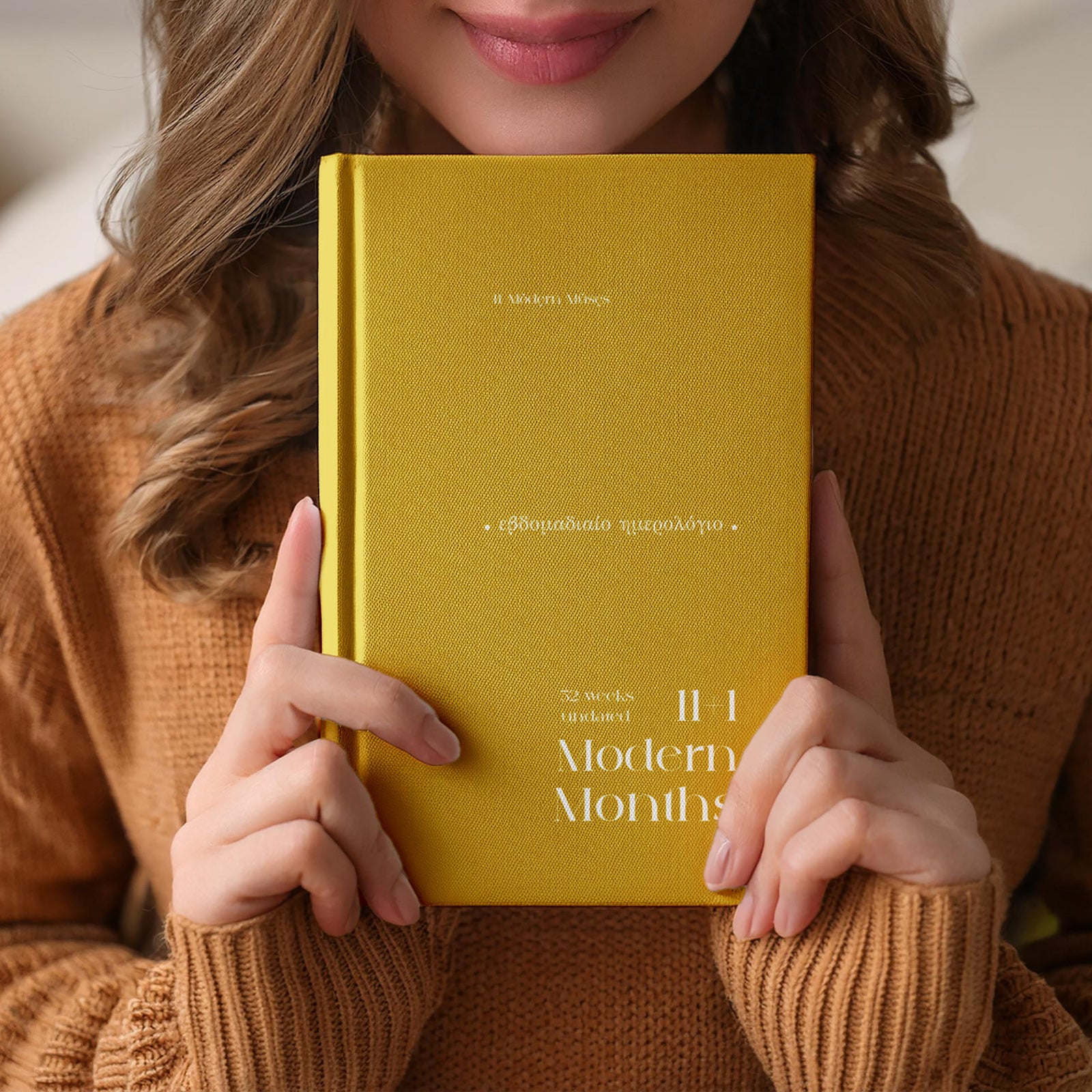 Girl holding a yellow undated planner titled '11+1Modern Months' with a blurred background